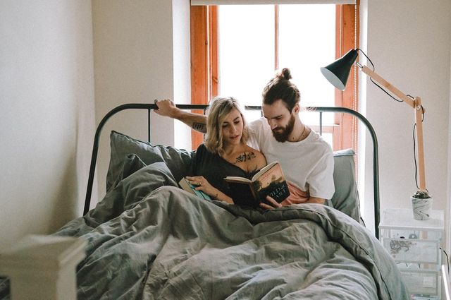 Los mejores edredones para mantenerte caliente todo el invierno, a young couple reading in bed, a comforter over them.